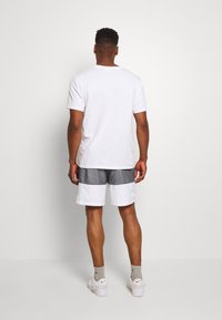 Vit bomull t-shirt i kombination med grå och vit färgblockerad shorts. Modell som bär vita sneakers och grå strumpor, sedd från ryggen.