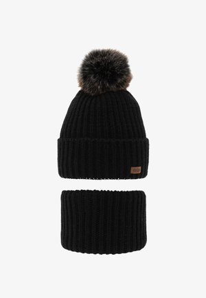 Cappello invernale nero a coste con grande pon pon di pelliccia e scaldacollo abbinato, entrambi caratterizzati da una piccola targhetta rettangolare marrone con il logo del marchio.