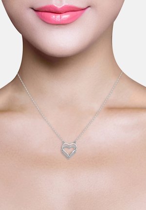 Silberne Herz-Halskette mit ineinander verwobenen Design, verziert mit kleinen klaren Edelsteinen, die an einer feinen Kette hängen und auf einem neutralen Hautton getragen werden.