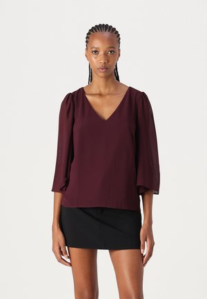 Burgundy blouse with a V-neck, three-quarter puff sleeves, and a relaxed fit. Material appears lightweight and smooth. Paired with a black skirt.