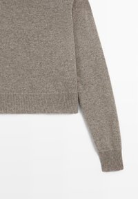 Maglione a maniche lunghe lavorato a maglia di colore marrone chiaro, con polsini e orlo a coste, esposto su uno sfondo bianco.