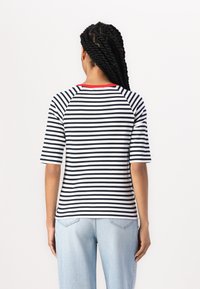 Gestreiftes T-Shirt in Schwarz und Weiß mit rotem Ausschnitt, mit einem lässigen Schnitt und kurzen Raglanärmeln, getragen mit hellblauen Jeans.