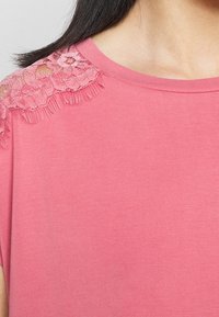 Top rosa a maniche corte con dettagli in pizzo sulle spalle, dalla texture liscia e con scollatura rotonda.