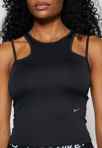 Donna che indossa un top atletico senza maniche nero con spalline scoperte e un piccolo logo Nike grigio vicino alla vita.