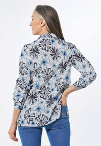Blumenhemd mit Knöpfen, das blaue und marineblaue Blumen auf einem hellgrauen Hintergrund zeigt. Langärmlig mit hochgekrempelten Ärmeln, klassischem Kragen und abgerundetem Saum.