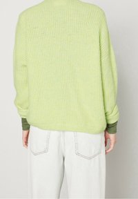 Maglione verde chiaro lavorato a maglia con finitura testurizzata, vestibilità oversize e maniche lunghe, abbinato a jeans di denim chiaro.