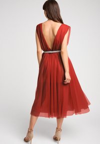 Czerwona sukienka z tiulu z głębokim dekoltem na plecach, krótkimi rękawami, skośną talią z ozdobnym srebrnym paskiem i zwiewną spódnicą sięgającą do połowy łydki.