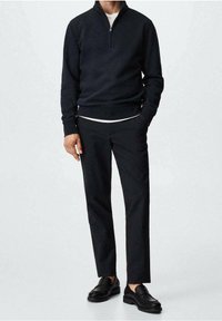 Pullover nero con mezza zip, tessuto strutturato, abbinato a pantaloni neri sartoriali e mocassini neri, che mette in risalto un outfit elegante e monocromatico.