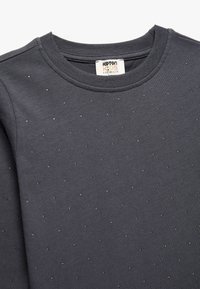 Grå sweatshirt med rund halsudskæring, der har små metalnitter jævnt fordelt hen over fronten. Blødt bomuldsstof.