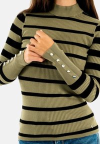 Olijfgroene geribbelde trui met zwarte horizontale strepen. Voorzien van knoopaccenten op de mouwen en een hoge halslijn. Getailleerd ontwerp.