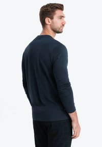 Mörkblå långärmad skjorta i mjukt tyg, med en enkel rund halsringning och åtsittande ärmar, kombinerad med rutiga byxor.