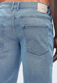 Ανοιχτό μπλε τζιν παντελόνι σε άτομο, ορατές πίσω τσέπες με ραφή σε σχήμα V και μια μπεζ ετικέτα στη μέση.