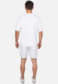 T-shirt bianca in cotone con maniche corte, abbinata a pantaloni corti bianchi. La maglietta presenta un collo rotondo e una vestibilità comoda.