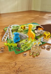 Colorful board game components including a yellow giraffe, blue zookeeper figure, green snake, dice, and various animal-shaped tokens against a wooden surface.