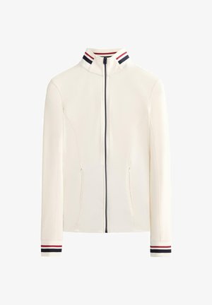 Fehér cipzáras kabát magas gallérral, a galléron és a mandzsettákon sötétkék és piros csíkos díszítéssel. Elöl két zsebével.