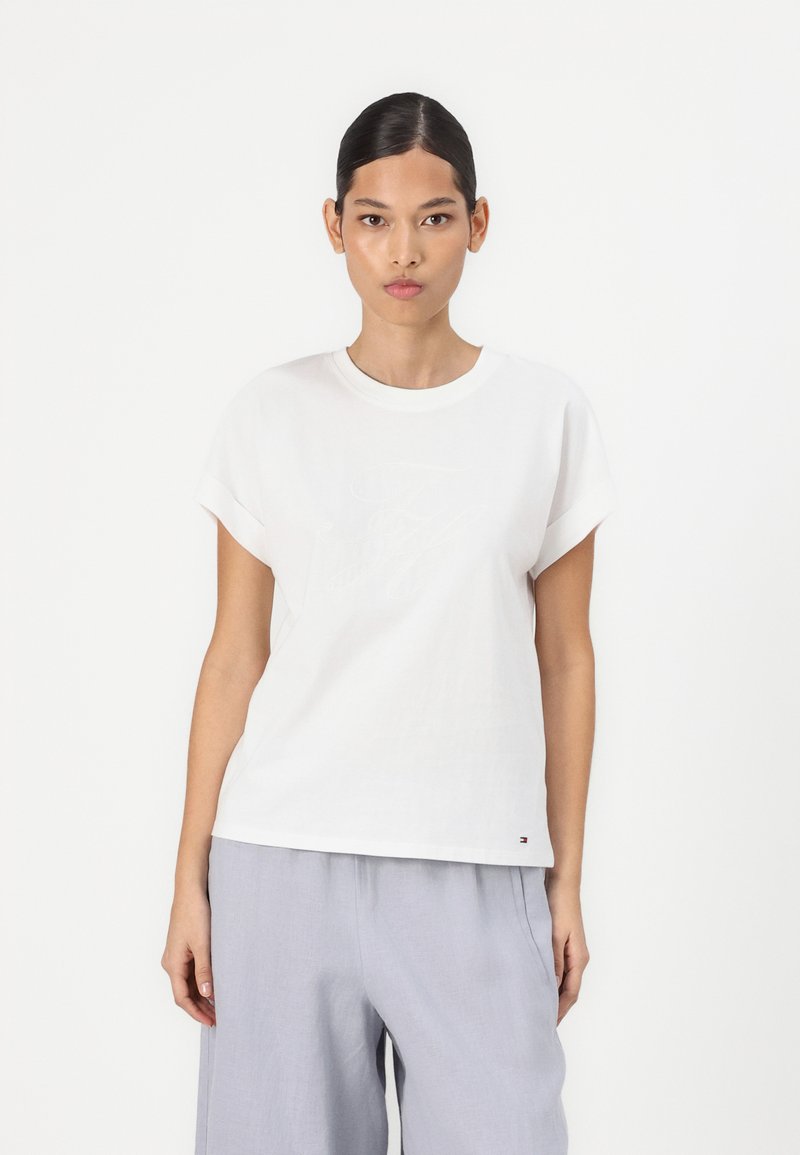 Witte katoenen T-shirt met opgerolde korte mouwen, met subtiele logo borduursels aan de voorkant en een klein logo-label aan de onderrand.
