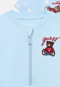 Ανοιχτό μπλε ζακέτα με φερμουάρ, διακοσμημένη με κέντημα αρκουδάκι σε κόκκινο και καφέ χρώμα με λογότυπο, υφασμάτινη με υφή και στρογγυλή λαιμόκοψη.