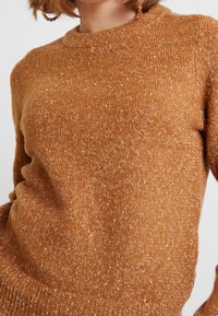 Brauner Strickpullover mit einer strukturierten, leicht flauschigen Oberfläche. Verfügt über einen Rundhalsausschnitt und lange Ärmel, die dezente Farbtupfer in helleren Tönen zeigen.