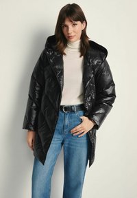 Czarna kurtka puchowa z kapturem, z pikowanym wzorem, błyszczącym wykończeniem i luźnym krojem. Połączona z jasnoniebieskimi spodniami o szerokich nogawkach.