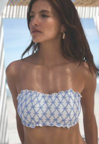 Witte bandeau bikini top met een blauw geborduurd geometrisch patroon, gerimpelde randen en een gladde stoffen textuur.