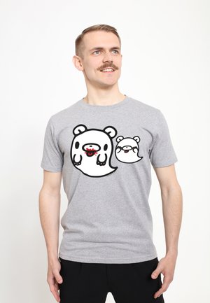 Mand med overskæg iført en grå t-shirt med to tegneseriebjørne spøgelser, en større og en mindre, på en ensartet hvid baggrund.