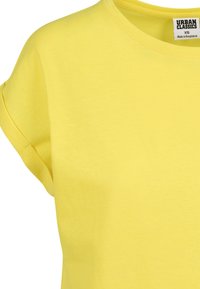 Gele katoenen T-shirt met korte opgerolde mouwen en een ronde hals; voorzien van een etiket met de tekst "URBAN CLASSICS," maat XS, gemaakt in Bangladesh.