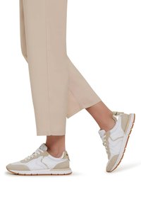 White and beige sneakers with suede accents and gold hardware. Lace-up design with a textured sole. Worn with cropped beige pants.