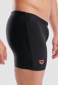 Schwarze Badehosen aus glattem Stoff, mit einem orangefarbenen "arena"-Logo auf der linken Seite und einer figurschmeichelnden Passform.