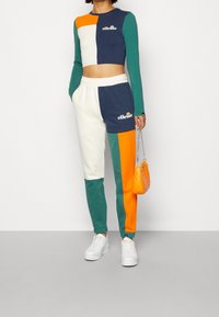 Värikäs tracksuit, jossa on lyhyt, monivärinen pitkähiha sekä yhteensopivat housut. Sisältää valkoisen joustavyöhön ja logoyksityiskohtia.