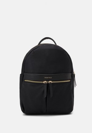 Sac à dos noir Anna Field avec poignée supérieure, poche avant zippée avec fermetures éclair dorées et design minimaliste sur fond blanc.
