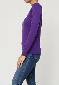 Pull violet à manches longues, avec des poignets et un ourlet côtelés, fabriqué dans un matériau doux, associé à un jean bleu ajusté.