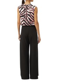Ärmellose Bluse mit pinken und schwarzen Zebra-Streifen, kombiniert mit weiten schwarzen Hosen mit Gesäßtaschen. Glatte Textur.