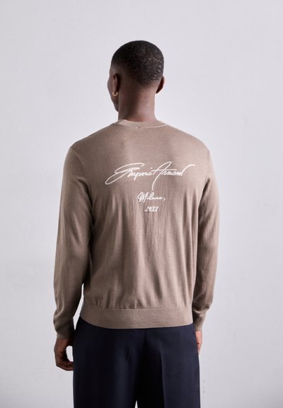 Brauner Strickpullover mit langen Ärmeln, Rundhalsausschnitt und gerippten Bündchen. Auf der Rückseite befindet sich weißer Signaturtext.