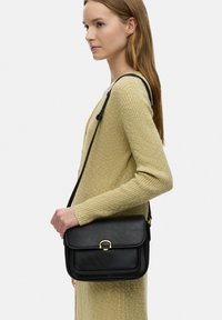 Borsa a tracolla nera in pelle con pattina, hardware dorato e design strutturato. Presenta una tracolla singola e una texture liscia.