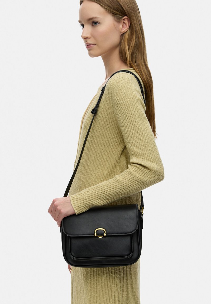 Borsa a tracolla nera in pelle con pattina, hardware dorato e design strutturato. Presenta una tracolla singola e una texture liscia.