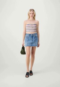 Top multicolore senza spalline in maglia con cordoncino, abbinato a una mini gonna di jeans azzurri con orlo sfrangiato e cuciture bianche. Sandali neri a scivolo e borsa verde.