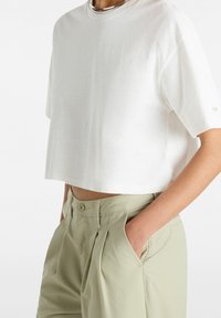 Vitt kort t-shirt med korta ärmar och rund halsringning. Parat med ljusgröna veckade byxor, synliga framfickor och knäppning.