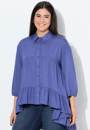Purple button-up blouse with a collar, featuring gathered details and a longer back hem. Made of lightweight fabric, with balloon sleeves.