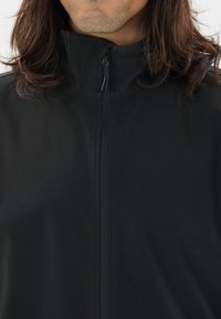 Schwarze Zip-Jacke mit hohem Kragen, aus strukturiertem Stoff gefertigt. Verfügt über einen durchgehenden Frontreißverschluss und sichtbare Nähdetails.