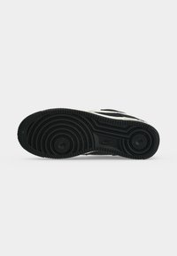 Μαύρη σόλα αθλητικού παπουτσιού Nike με κυκλικό σχέδιο πέλματος και ορατό λογότυπο Nike σε απλό λευκό φόντο.