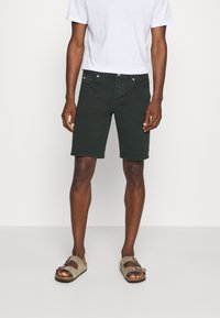 Ciemnozielone szorty z denimu o klasycznym kroju, z pięcioma kieszeniami i subtelną fakturą, zestawione z prostą białą koszulką i beżowymi sandałami.