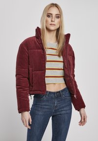 Burgunderfarget kordfløyels pufferjakke med høy krage, forkortet design og glidelås. Kombinert med en gråstripet crop top og mørke jeans.