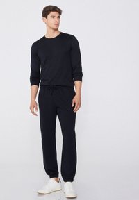 Schwarzes Langarmshirt und passende Jogginghose mit Kordelzugbund, aus weichem Stoff; kombiniert mit weißen Sneakers. Einfaches Design, ohne Muster.