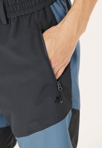 Herrshorts i svart och blå färgkombination. Har en ficka med dragkedja och resårmidja, tillverkade av lätt och andningsbart material.