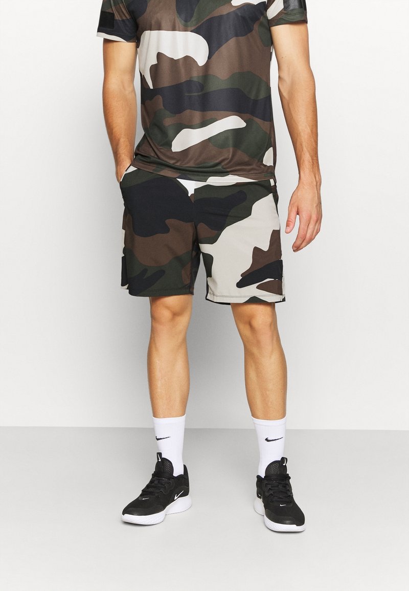 Sportovní kraťasy s kamuflážním vzorem v tmavě zelené, černé a béžové barvě. Kombinované s ladící kamuflážovou košilí a černými teniskami s bílými akcenty.