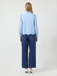 Light blue shirt with embroidered cut-out patterns at the back, paired with high-waisted dark blue wide-leg jeans and white heels.