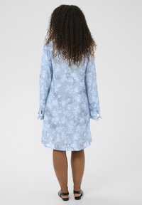 Hellblaues Blumenkleid mit langen Ärmeln, weitem Schnitt und Bindebändern an den Manschetten. Weiches Material mit zartem Blumenmuster.