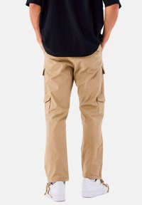 Beige cargo bukser med sidelommer, lige ben og et holdbart stof. Båret med en sort skjorte og hvide sneakers.