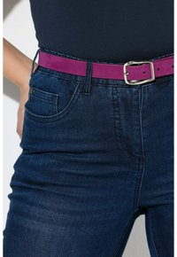 Dunne donkerblauwe denim jeans met een voorzak, gecombineerd met een brede fuchsia riem met een zilveren metalen gesp en een bijpassende pen.
