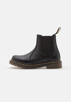 Botte Chelsea en cuir noir avec panneau latéral élastique, surpiqûres jaunes, languette de tirage et semelle rainurée, vue de côté extérieur sur fond blanc.